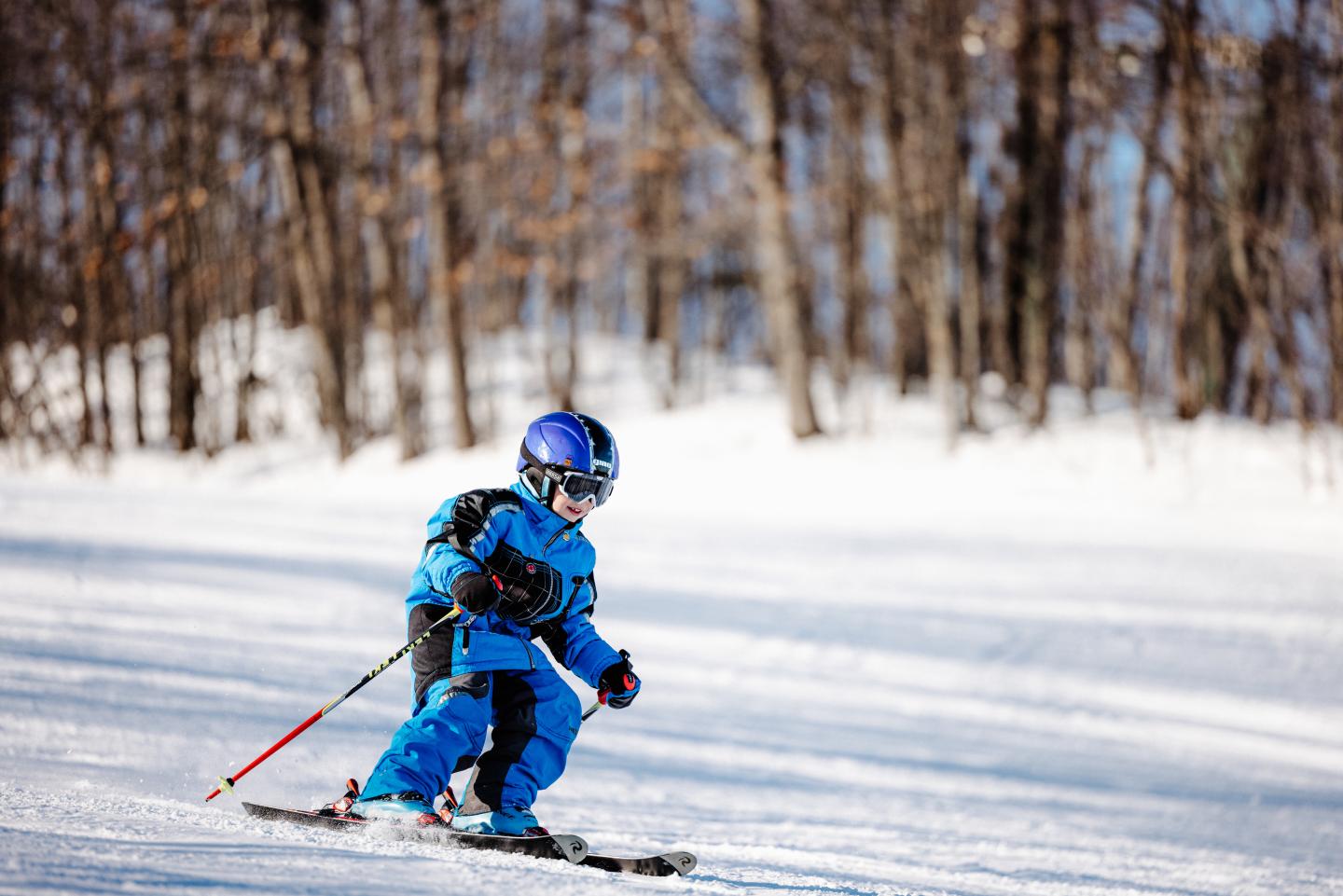 Child skiing downhill in blue gear on a sunny day.