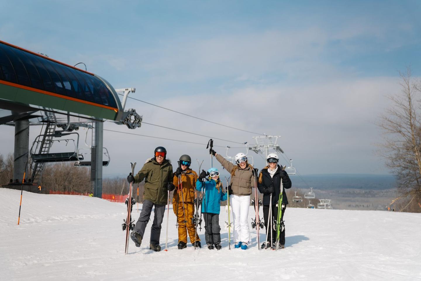 A group of skiers poses on a snowy slope near a ski lift under a partly cloudy sky.