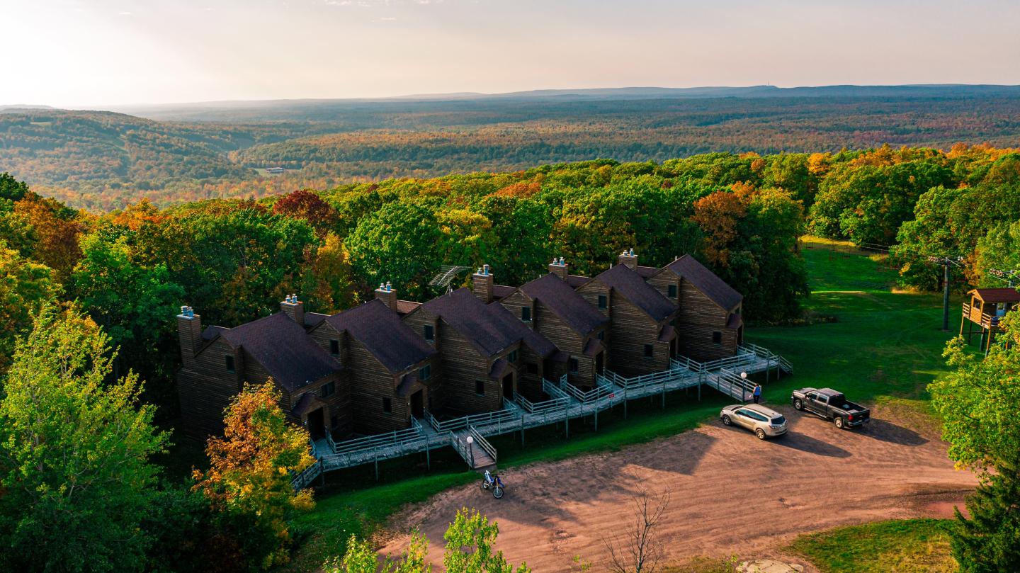 Row of cabins among trees, vibrant autumn foliage, clear sky.