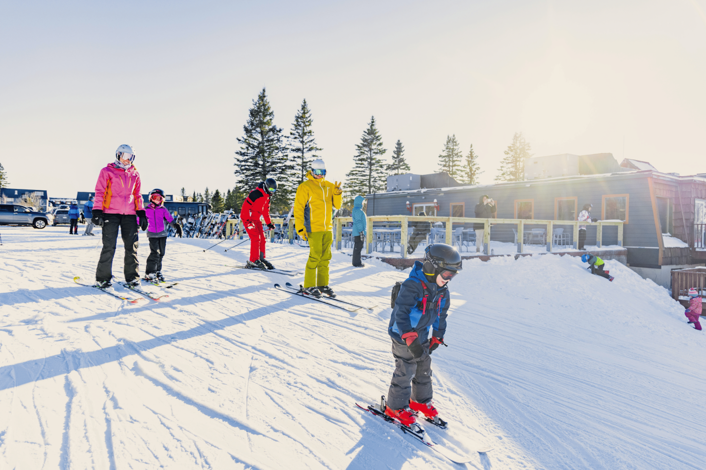 Children skiing on a sunny, snow-covered slope near a lodge.