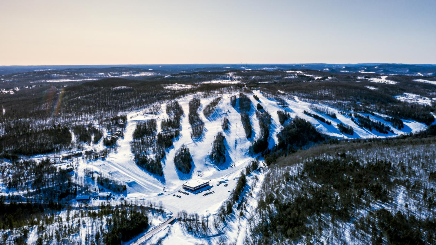 Aerial view of snow-covered ski slopes winding through a forested mountain.